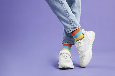 Photo of Woman in stylish colorful socks, sneakers and jeans on violet background, closeup. Space for text