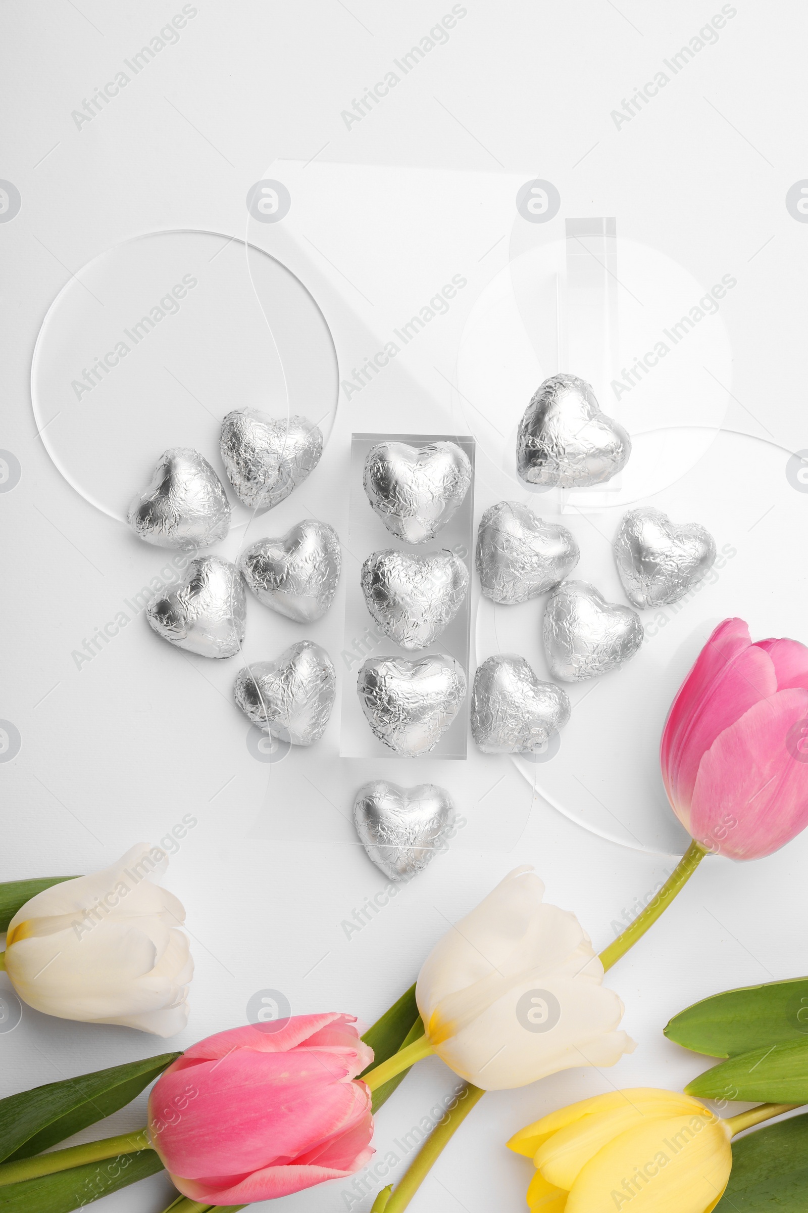 Photo of Heart made with delicious chocolate candies and beautiful tulips on white background, top view