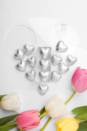 Photo of Heart made with delicious chocolate candies and beautiful tulips on white background, top view