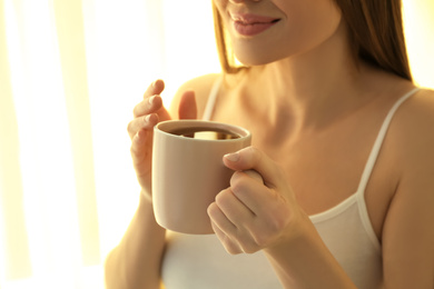 Photo of Young woman with cup near window at home, closeup. Lazy morning