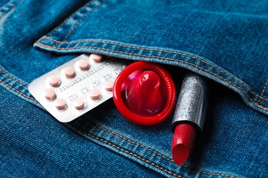 Photo of Red lipstick with condom and birth control pills in pocket of jeans, closeup. Safe sex concept