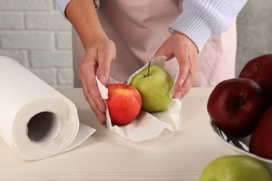 Photo of Woman wiping apples with paper towel at light wooden table, closeup