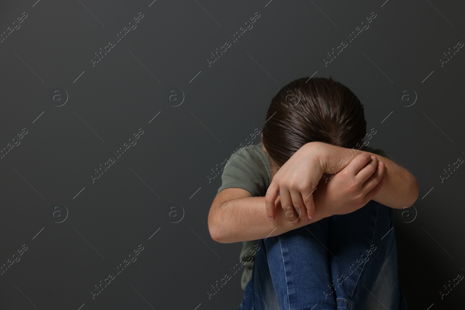 Photo of Child abuse. Upset girl sitting on floor near grey wall, space for text