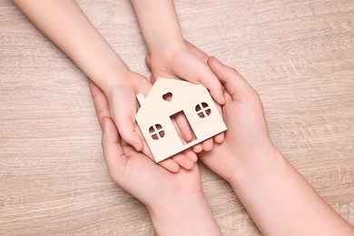 Photo of Home security concept. Man with his little child holding house model at wooden table, top view