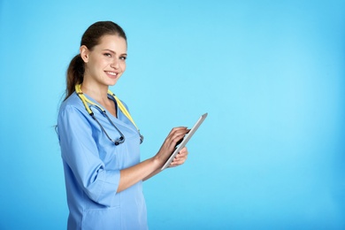 Portrait of young medical assistant with stethoscope and tablet on color background. Space for text