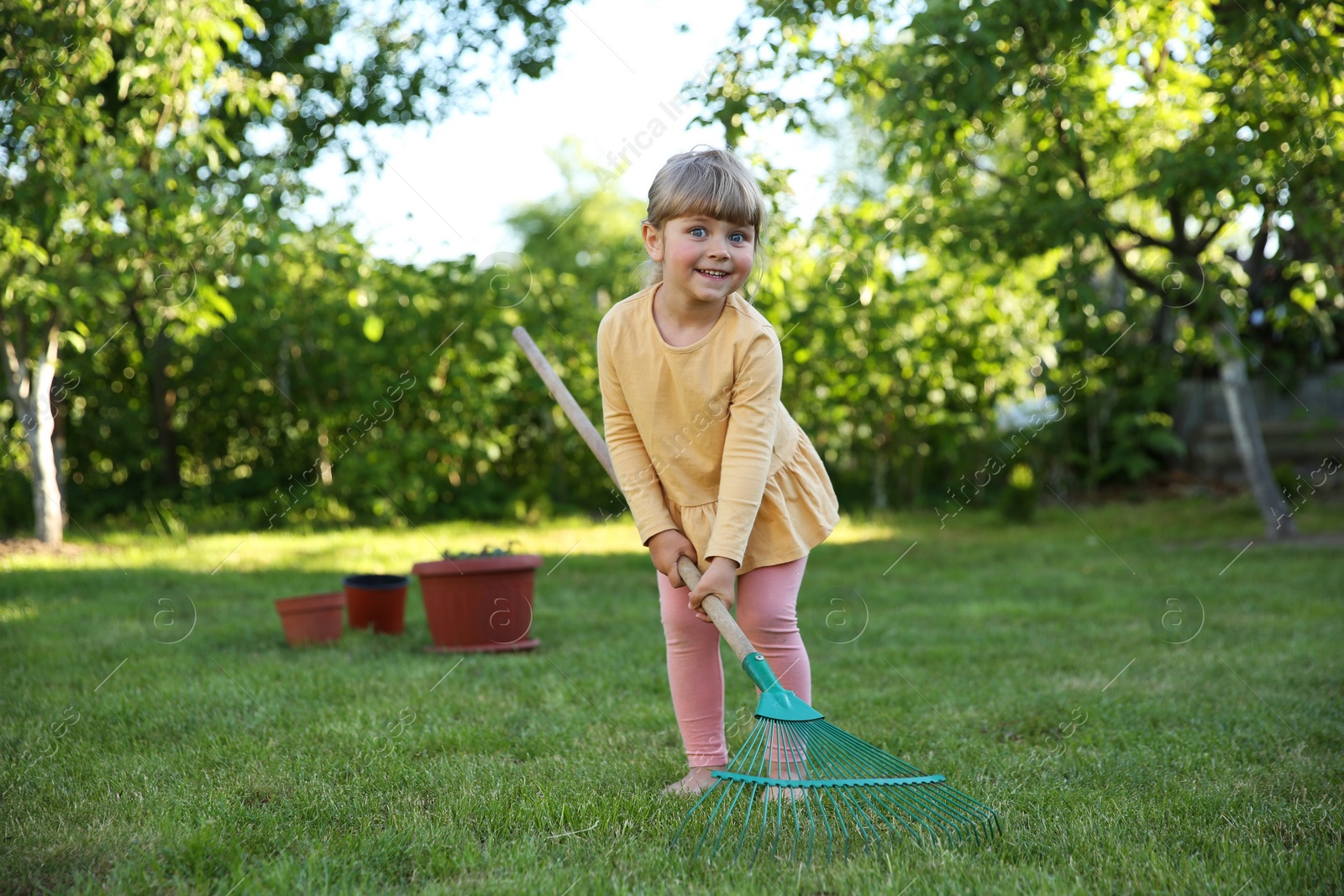 Photo of Cute little girl with rake in garden on spring day