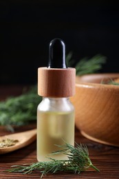 Photo of Bottle of essential oil and fresh dill on wooden table