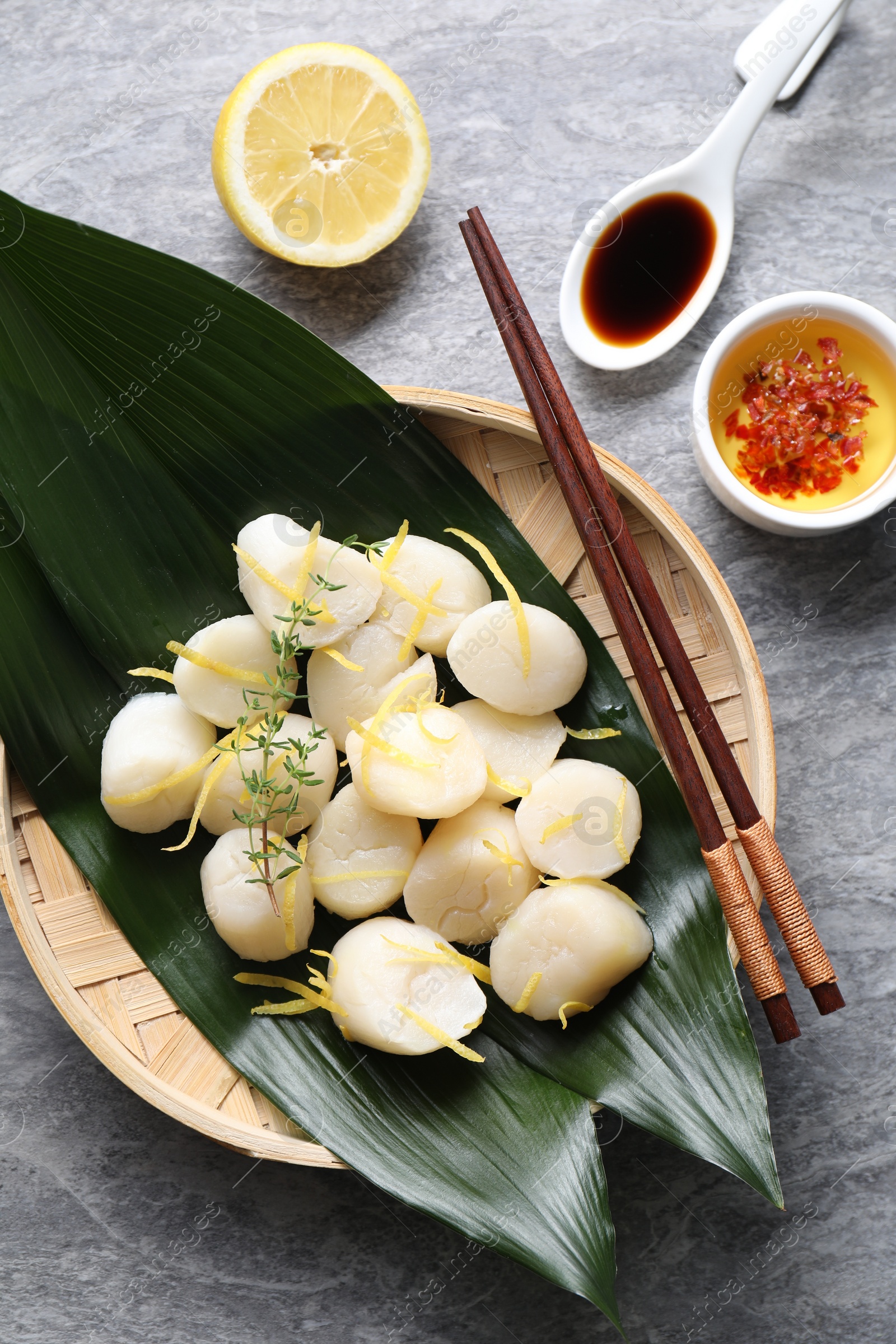 Photo of Raw scallops with thyme, lemon zest and sauces on grey marble table, flat lay