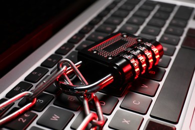 Photo of Cyber security. Metal combination padlock with chain on laptop, closeup