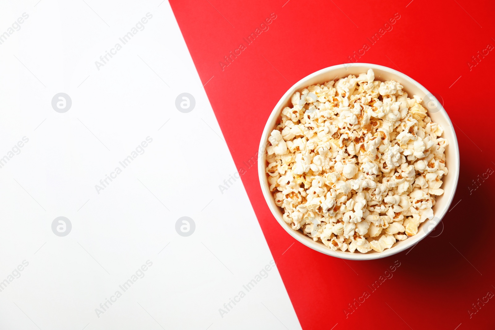 Photo of Tasty popcorn in paper cup and space for text on color background, top view. Cinema snack