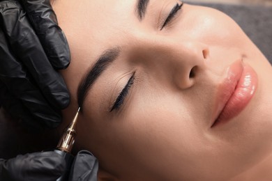 Photo of Young woman undergoing procedure of permanent eyebrow makeup in tattoo salon, closeup