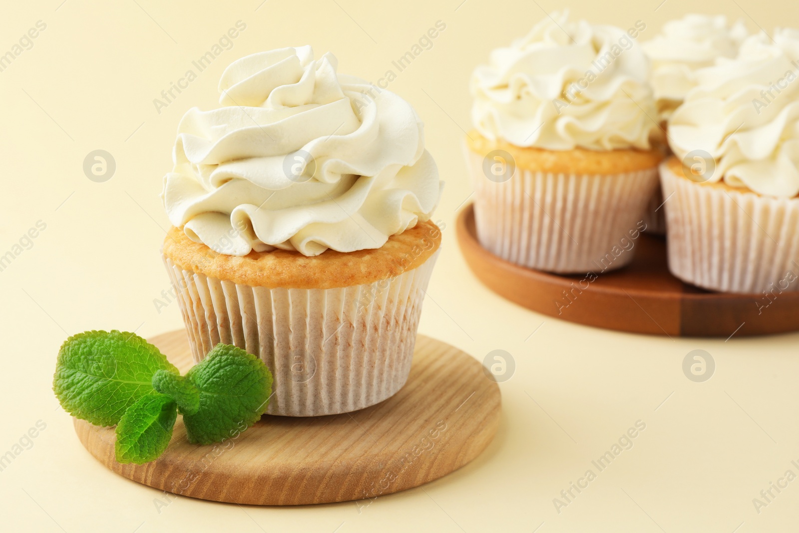 Photo of Tasty vanilla cupcakes with cream and mint on pale yellow background, closeup