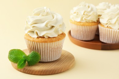 Photo of Tasty vanilla cupcakes with cream and mint on pale yellow background, closeup