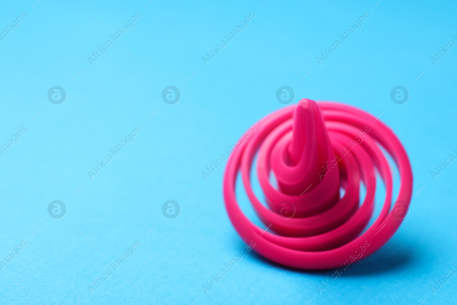 Photo of One pink spinning top on light blue background, closeup,. Space for text