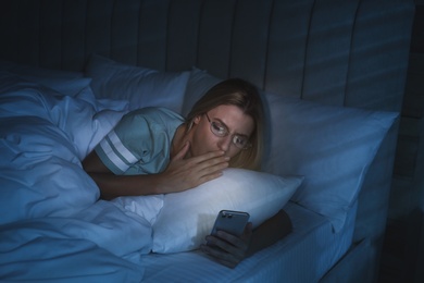 Young woman using smartphone in bed at night. Nomophobia and sleeping disorder problem