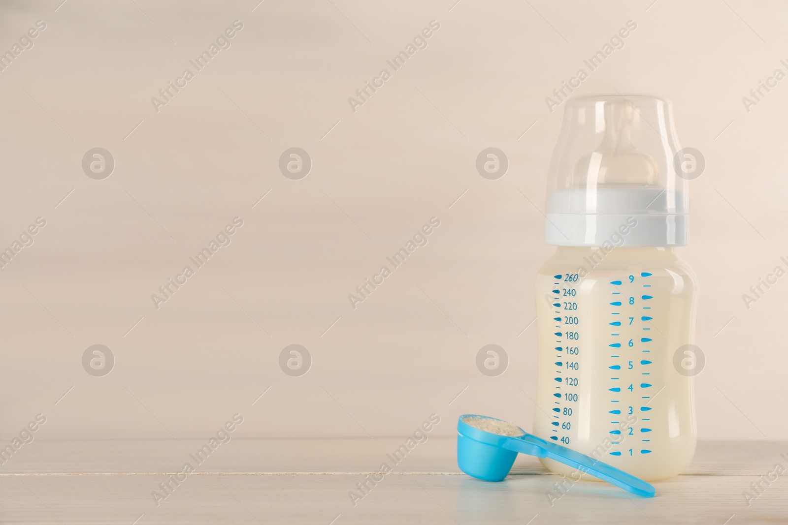 Photo of Feeding bottle with infant formula and powder on white wooden table, space for text