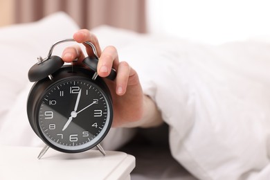 Photo of Man turning off alarm clock in bedroom, focus on hand. Space for text