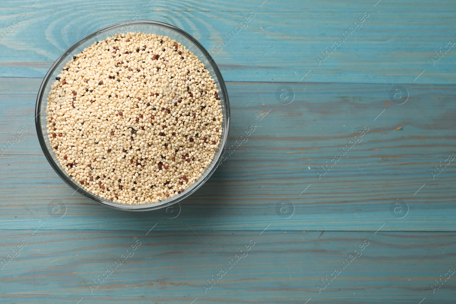 Photo of Raw quinoa seeds in bowl on light blue wooden table, top view. Space for text