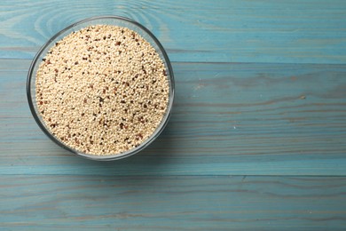 Photo of Raw quinoa seeds in bowl on light blue wooden table, top view. Space for text