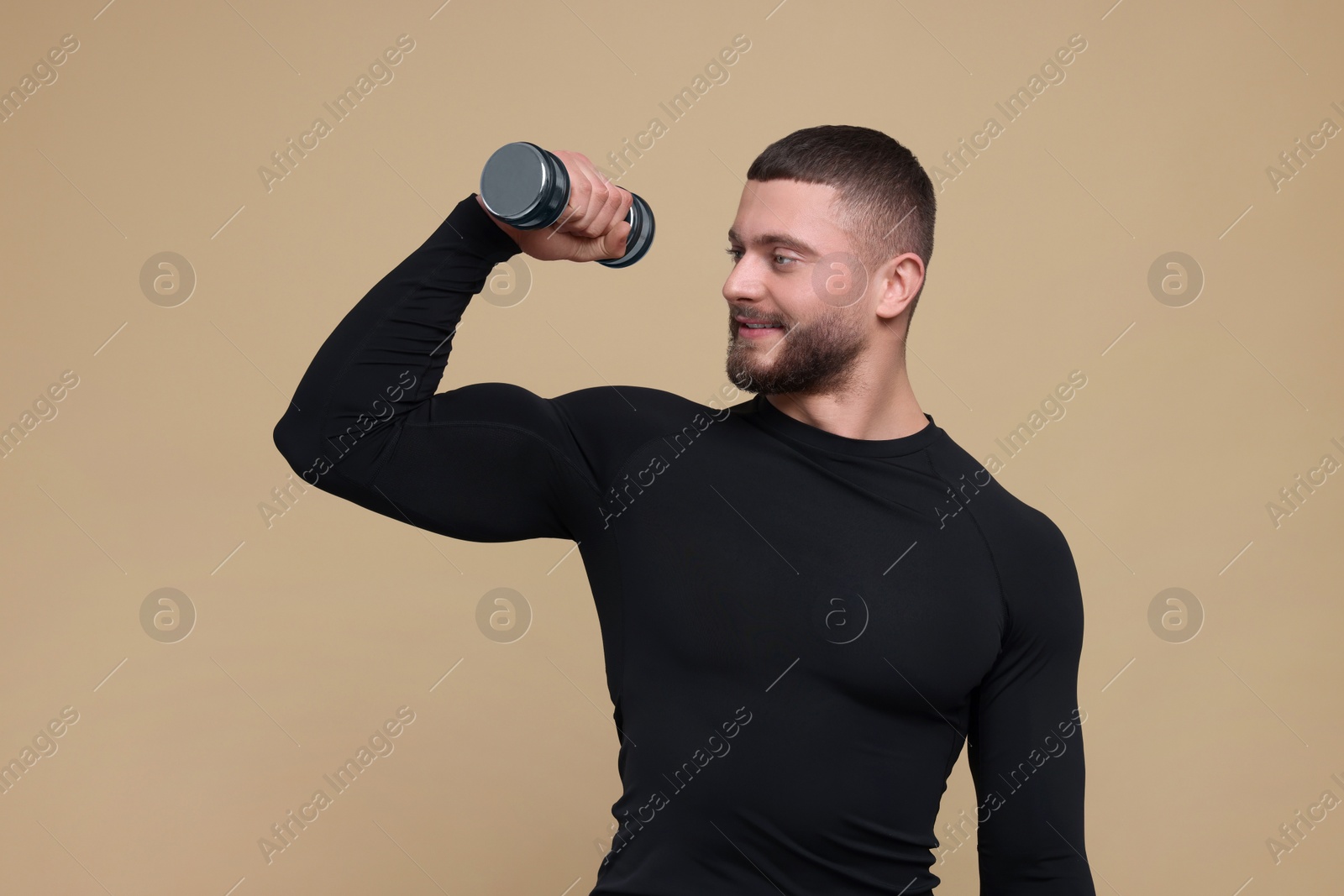 Photo of Handsome sportsman exercising with dumbbell on brown background