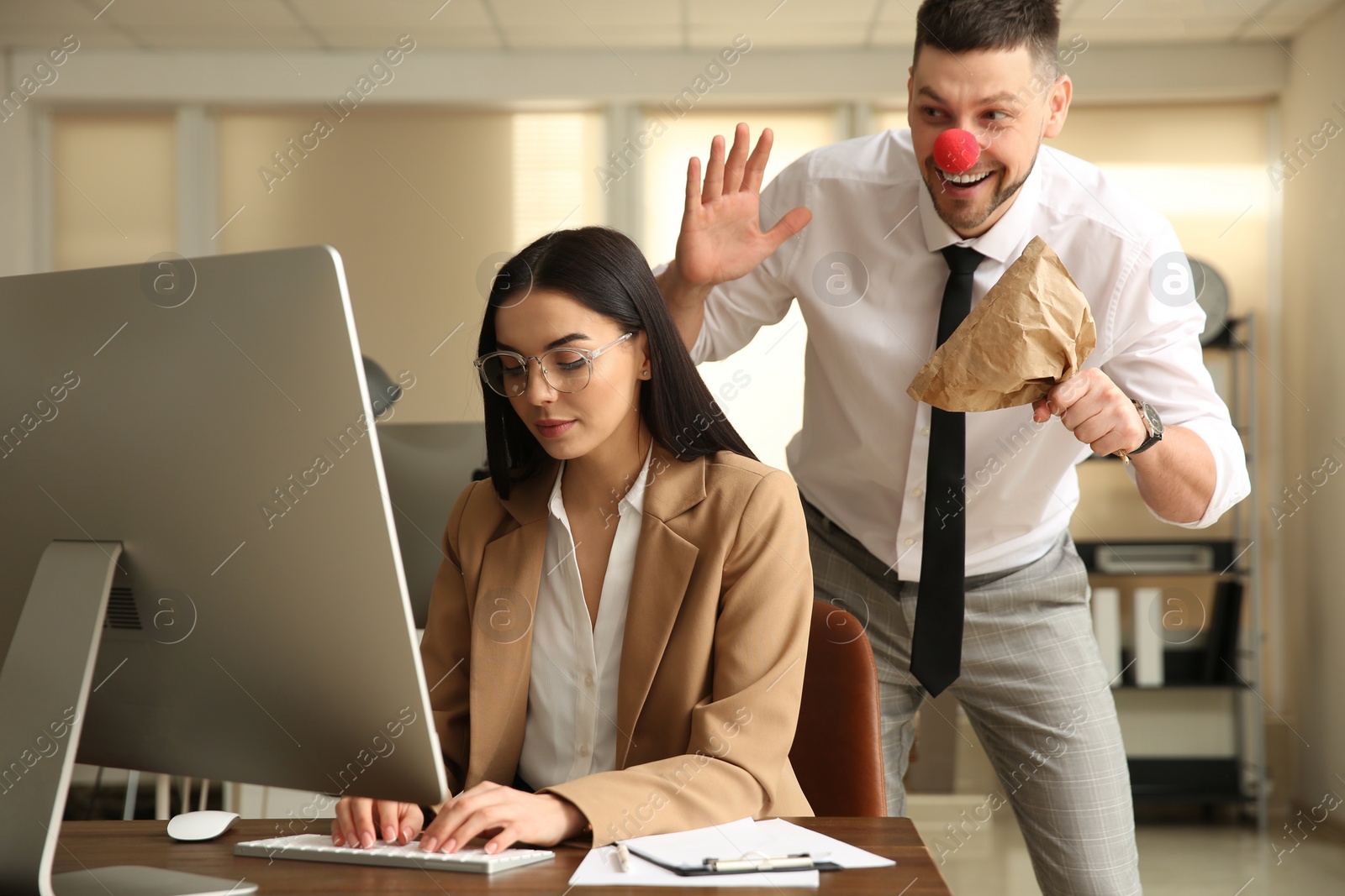 Photo of Man popping paper bag behind his colleague in office. Funny joke