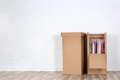 Photo of Wardrobe boxes with clothes against brick wall indoors. Space for text