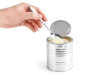 Woman pouring condensed milk from spoon into tin can on white background, closeup. Dairy product