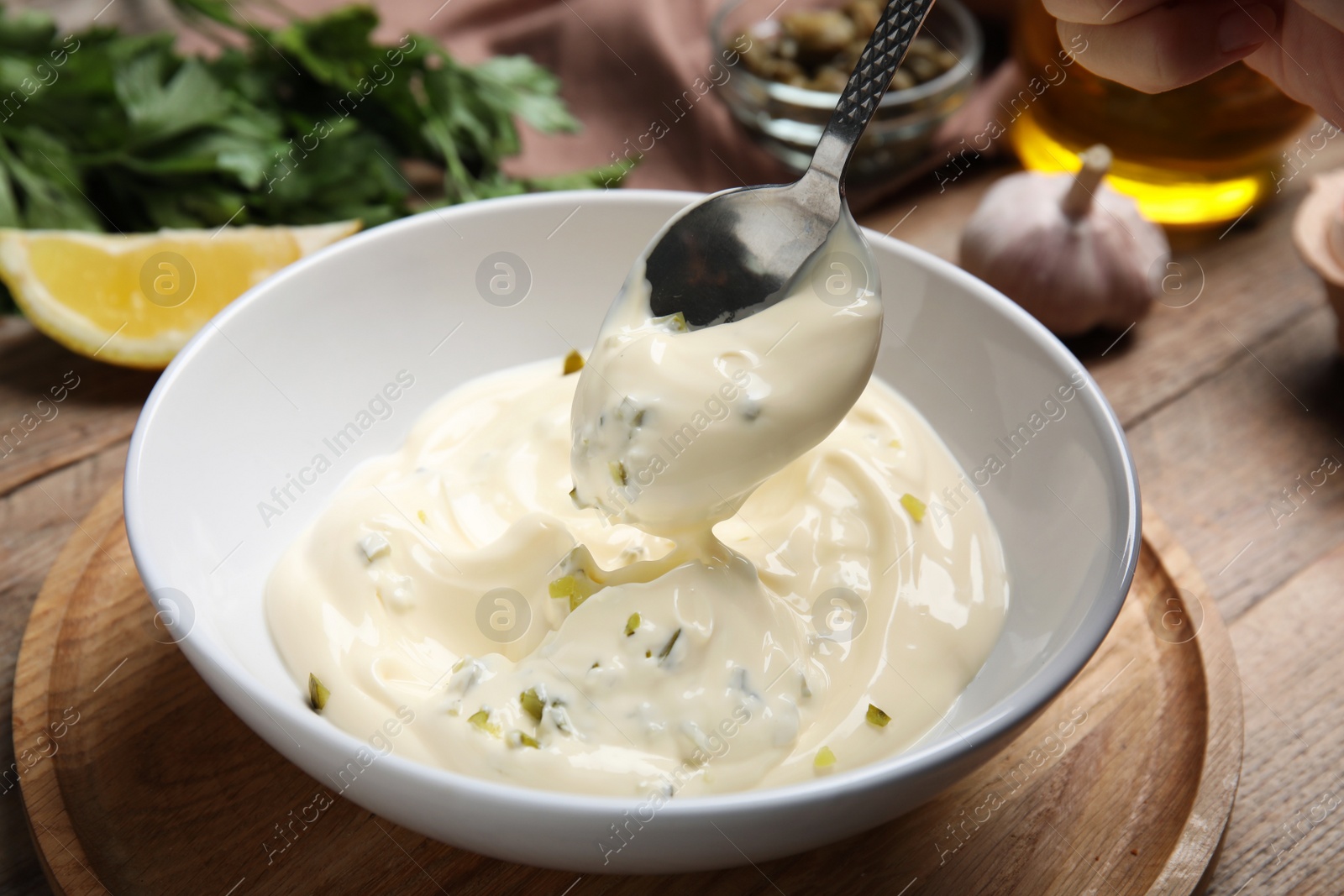 Photo of Delicious tartar sauce and spoon on wooden table, closeup