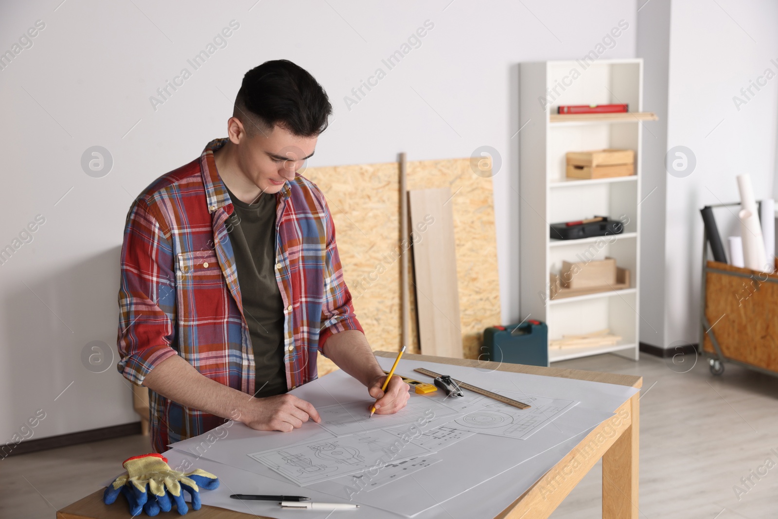 Photo of Young handyman working with blueprints at table in room