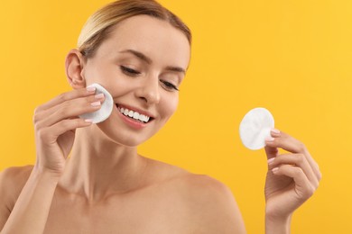 Photo of Smiling woman removing makeup with cotton pads on yellow background