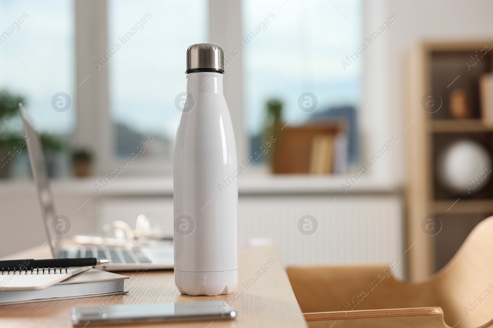 Photo of White thermos bottle at wooden table indoors