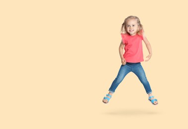 Cute girl jumping on beige background, space for text