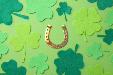 St. Patrick's day. Golden horseshoe and decorative clover leaves on green background, flat lay