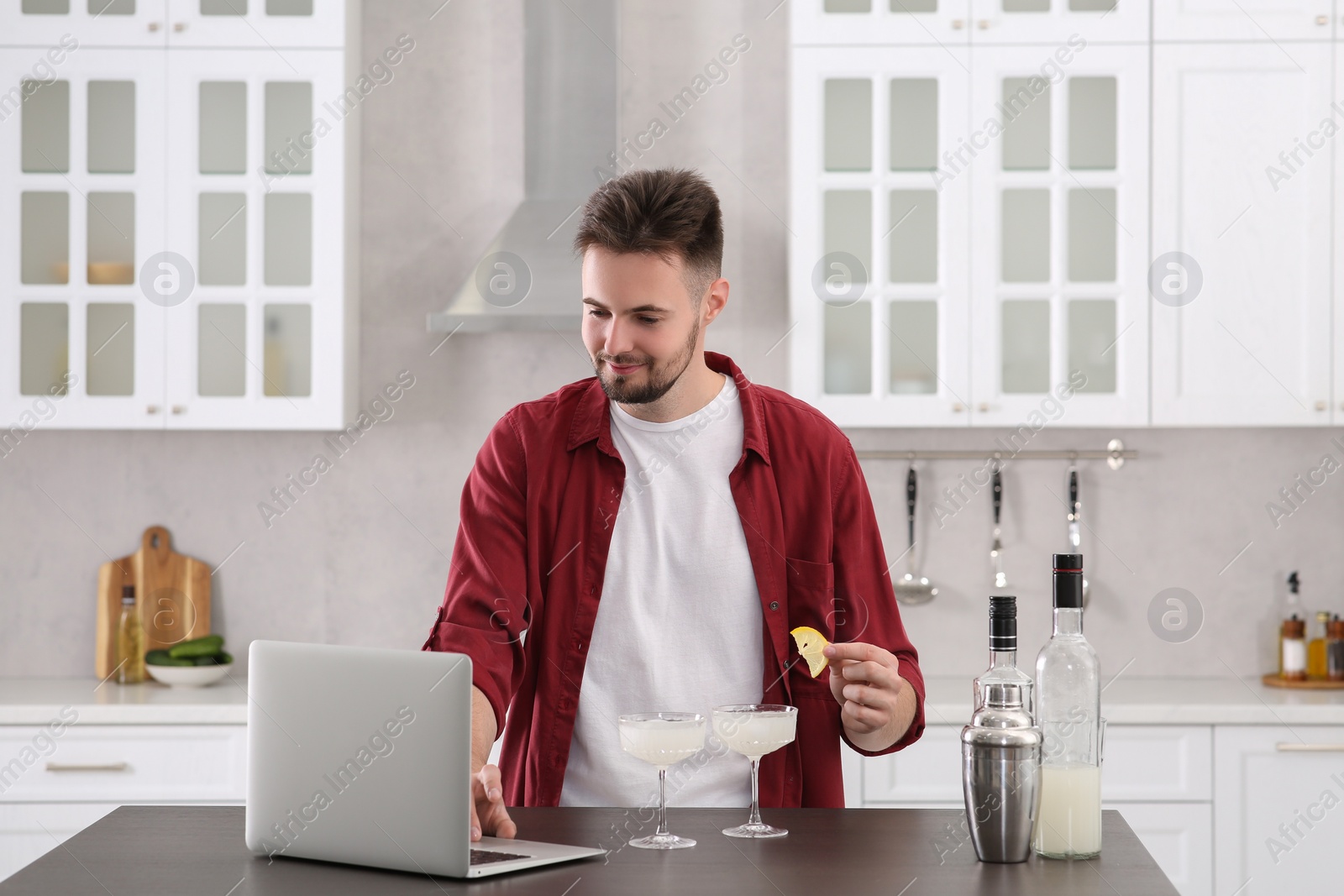 Photo of Man learning to make cocktail with online video on laptop at table in kitchen. Time for hobby