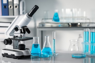 Different laboratory glassware, test tubes with light blue liquid and microscope on table