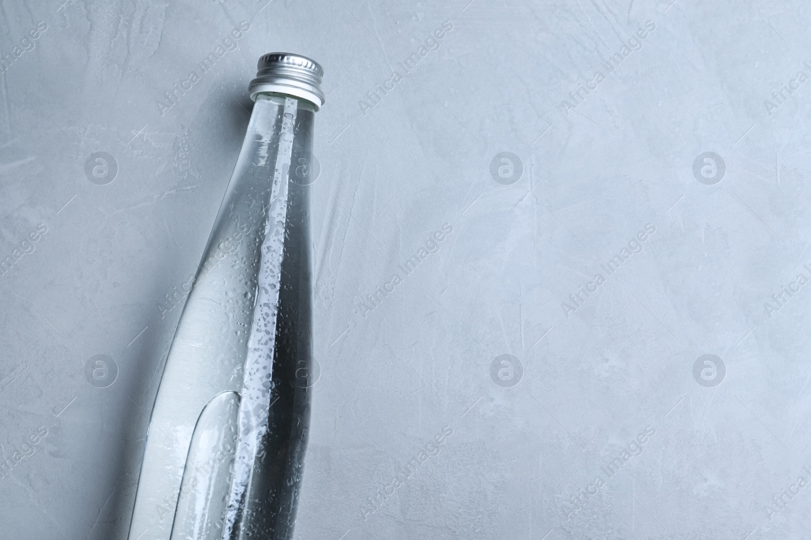 Photo of Glass bottle with water on light grey background, top view. Space for text