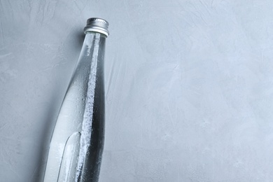 Glass bottle with water on light grey background, top view. Space for text