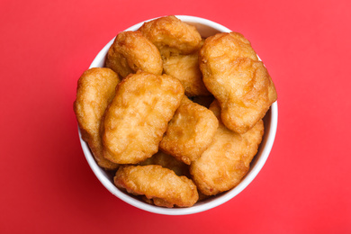 Bucket with delicious chicken nuggets on red background, top view