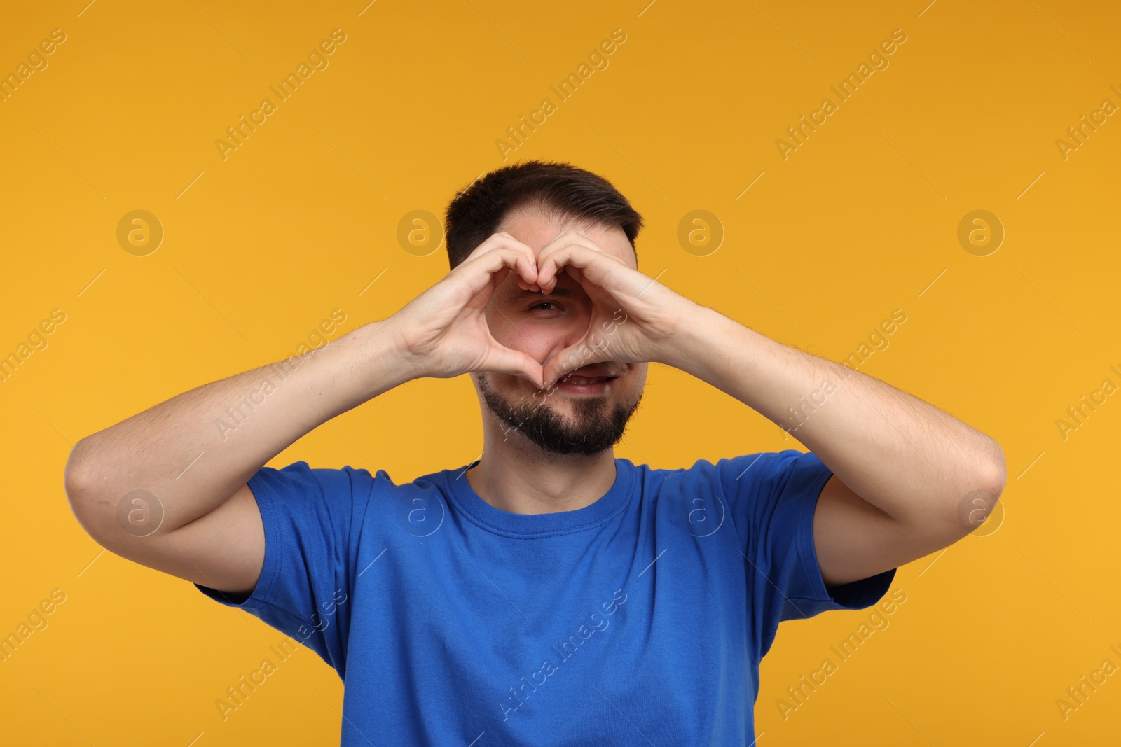 Photo of Man looking through folded in shape of heart hands on golden background