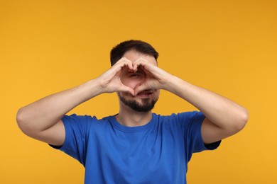 Photo of Man looking through folded in shape of heart hands on golden background