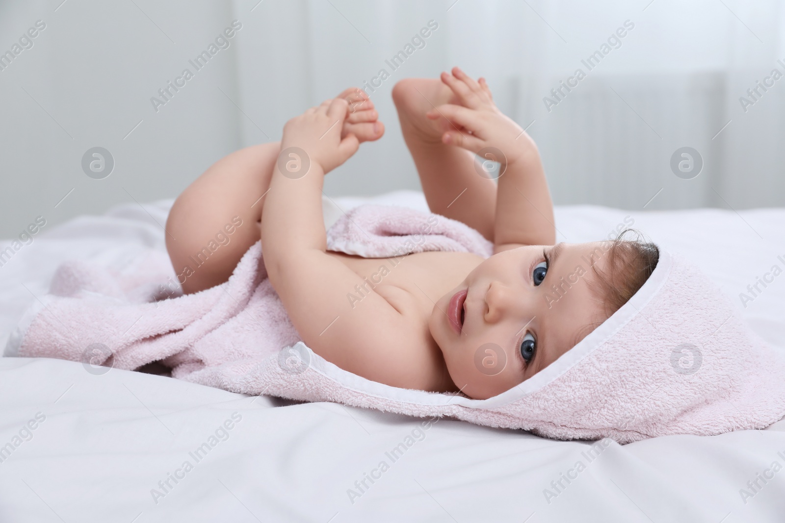 Photo of Cute little baby in hooded towel after bathing on bed at home