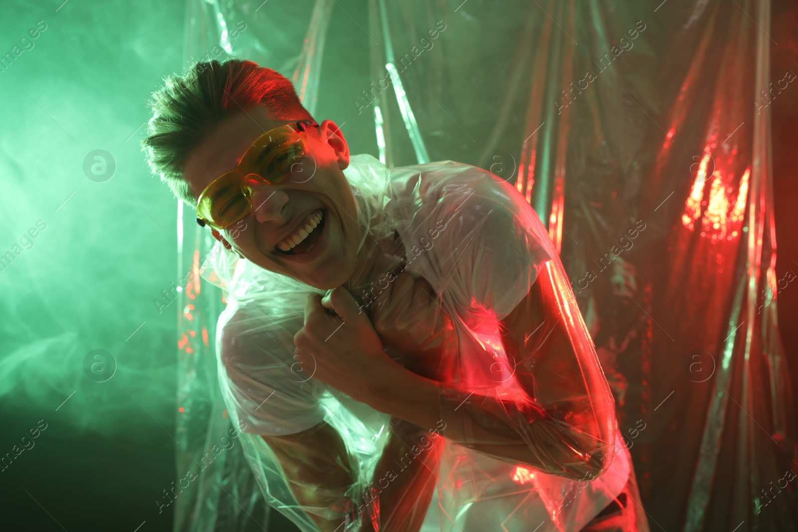 Photo of Stylish young man wearing clear coat and glasses in neon lights