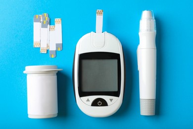 Photo of Digital glucometer, lancet pen and test strips on light blue background, flat lay. Diabetes control