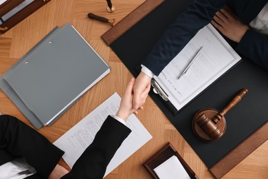 Photo of Notary shaking hands with client at wooden table, top view