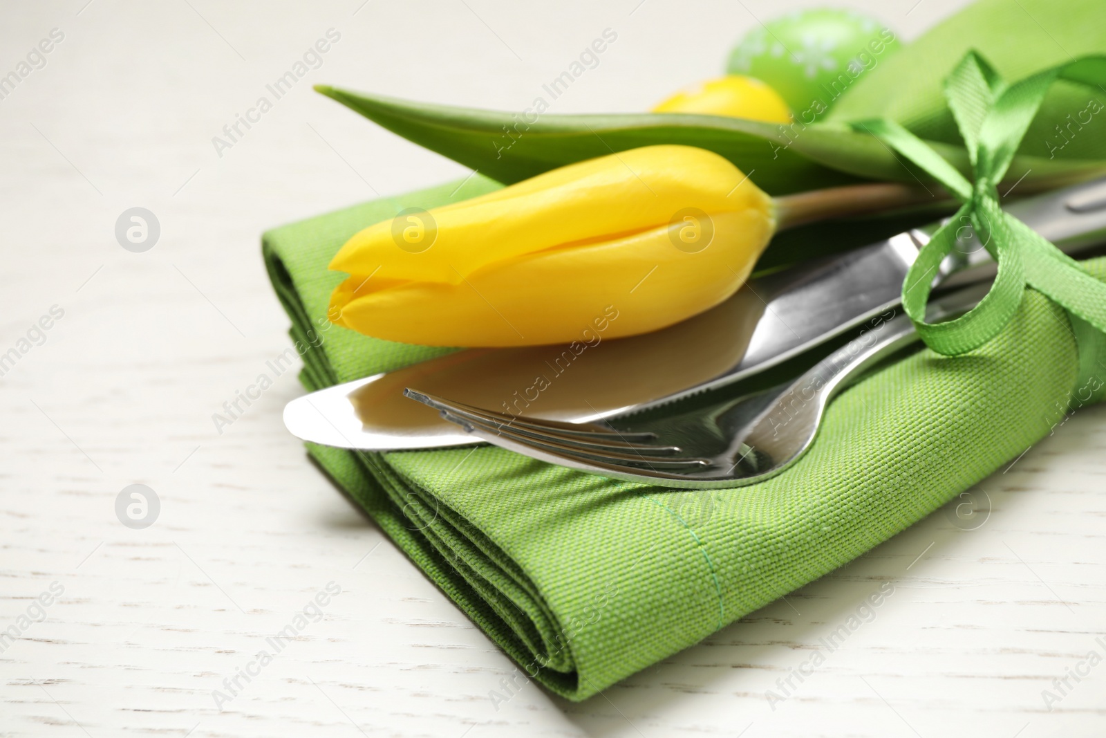 Photo of Cutlery set with beautiful tulip on white wooden table, closeup. Easter celebration