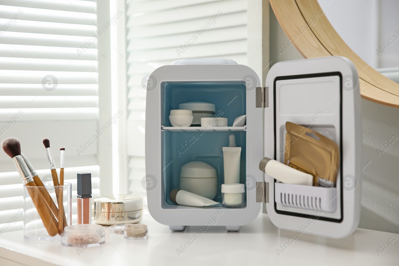 Photo of Cosmetics refrigerator and skin care products on white vanity table indoors