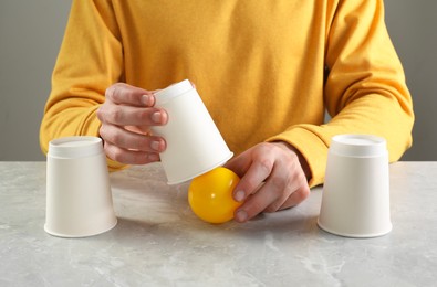 Photo of Shell game. Man showing ball under cup at light marble table, closeup
