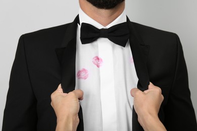 Photo of Woman grabbing her husband by suit jacket due to lipstick kiss marks on his shirt, closeup