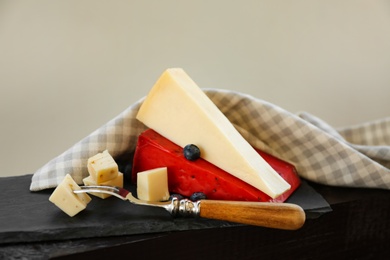 Photo of Different types of delicious cheeses and fork on slate plate, closeup