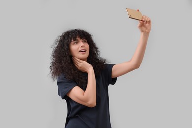 Beautiful young woman taking selfie on light grey background